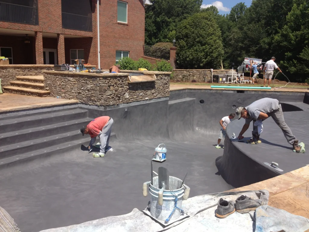 Workers plastering the interior of a residential swimming pool during renovation.